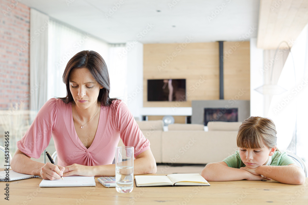 Mother sitting at table with daughter, using calculator Mother sitting at table with daughter, using calculator