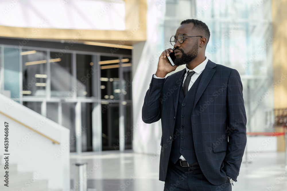 Young elegant businessman communicating on mobile phone while standing in contemporary business center Young elegant businessman communicating on mobile phone while standing in contemporary business center