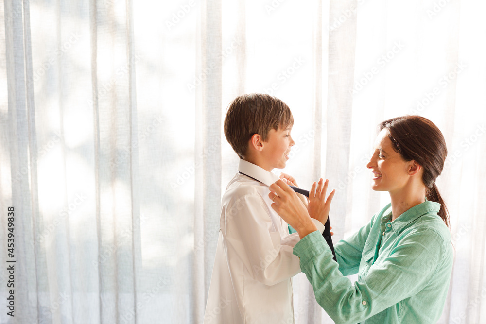 Obraz premium Mother tying son's tie at window
