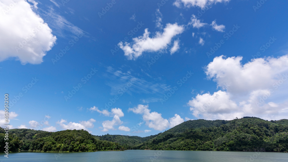 White clouds in blue sky over green mountains covered with rainforests trees Beautiful landscape of Mountain and Lake with reflex in the water scenery beautiful view with blue sky and white clouds.