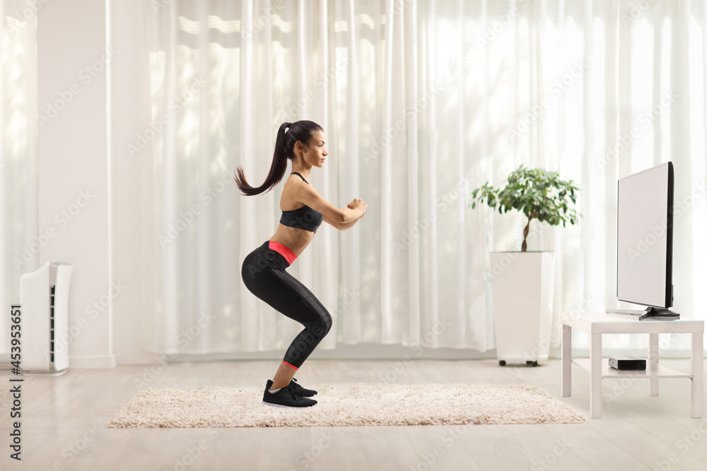 Full length profile shot of a young slim woman exercising in front of tv Full length profile shot of a young slim woman exercising in front of tv