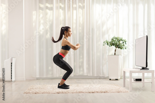 Full length profile shot of a young slim woman exercising in front of tv