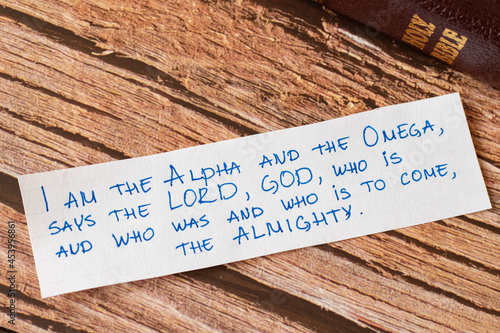 God Jesus Christ is the I AM, Alpha and Omega, First and Last, the LORD Almighty. Closeup of handwritten message on wooden background with closed Bible. Biblical concept book of Revelation. photo