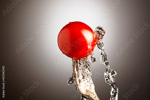 ripe cherry tomato on a metal fork. Splashes of water. Black white gradient background