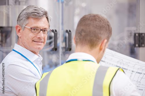 Supervisor and worker reading blueprints in factory