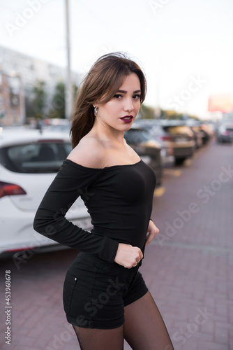 Beautiful young model girl in a black dress with long hair posing in the evening in the city 