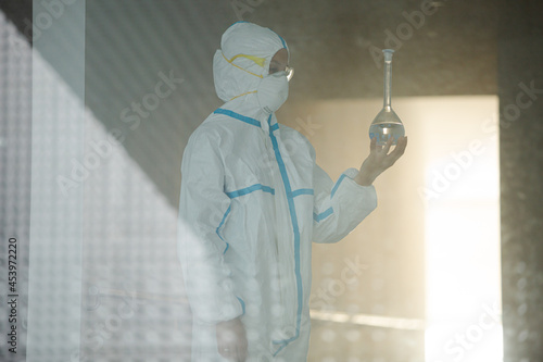 Scientist in clean suit examining liquid in test tube