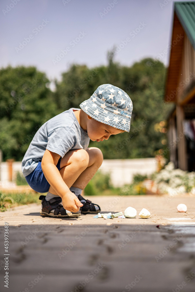 Cheerful little boy drawing hopscotch with chalk on ground enjoying happy childhood at backyard Cheerful little boy drawing hopscotch with chalk on ground enjoying happy childhood at backyard