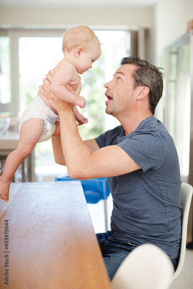 Fototapeta premium Father helping baby walk on table