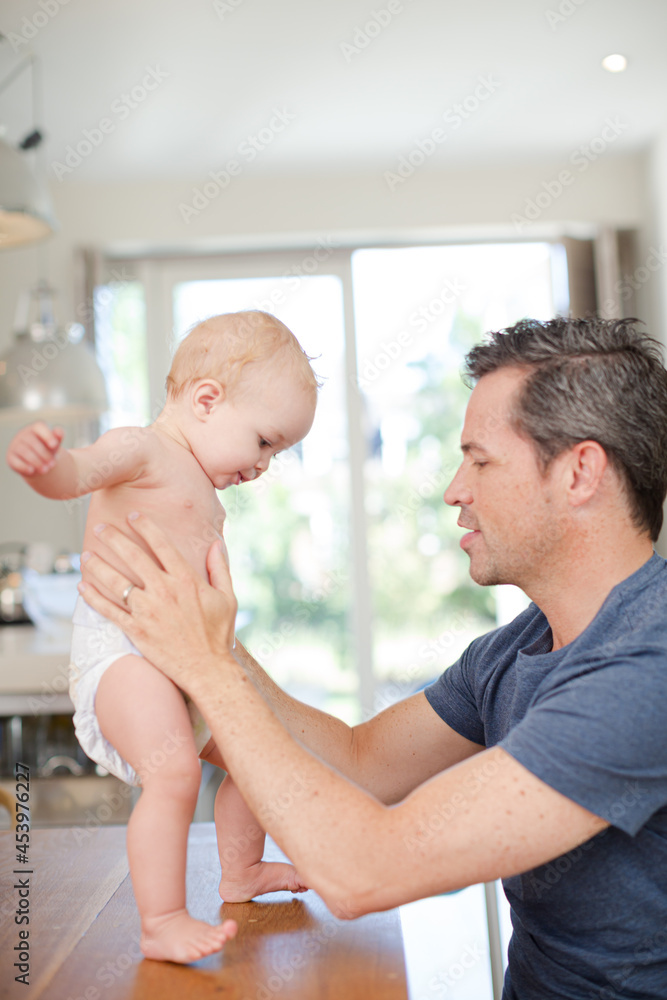 Father helping baby walk on table Father helping baby walk on table