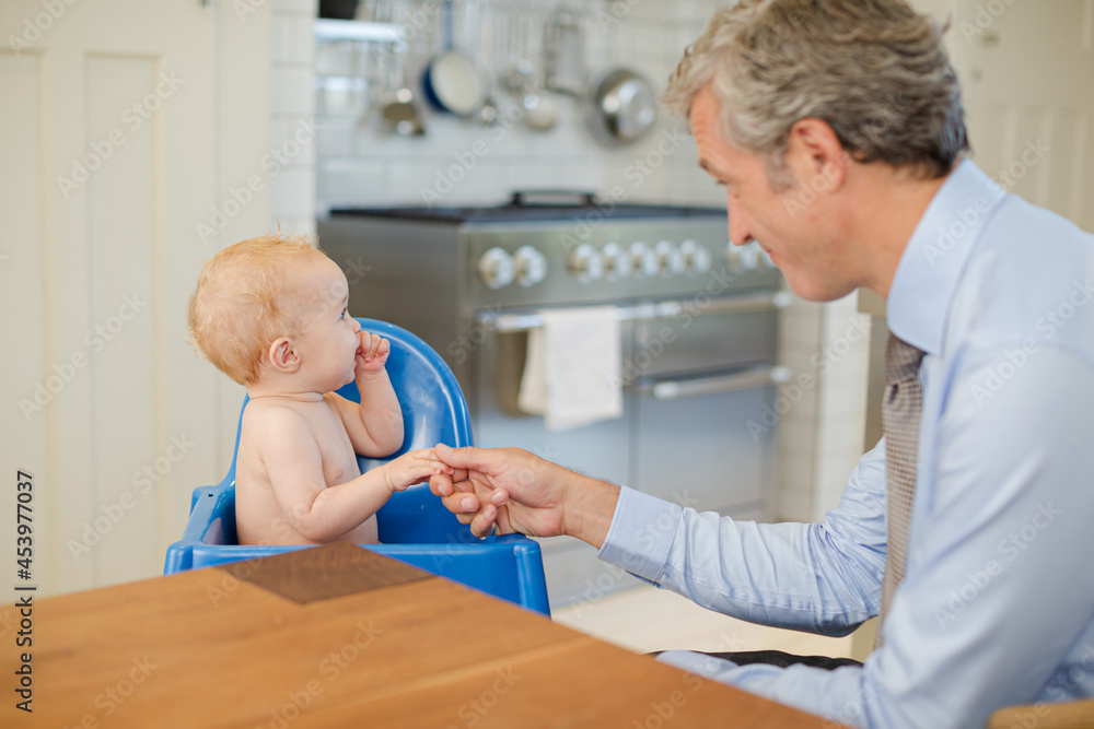 Fototapeta premium Father playing with baby in high chair