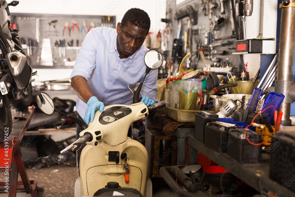 Male afro american worker repairing scooter in motorcycle workshop. High quality photo