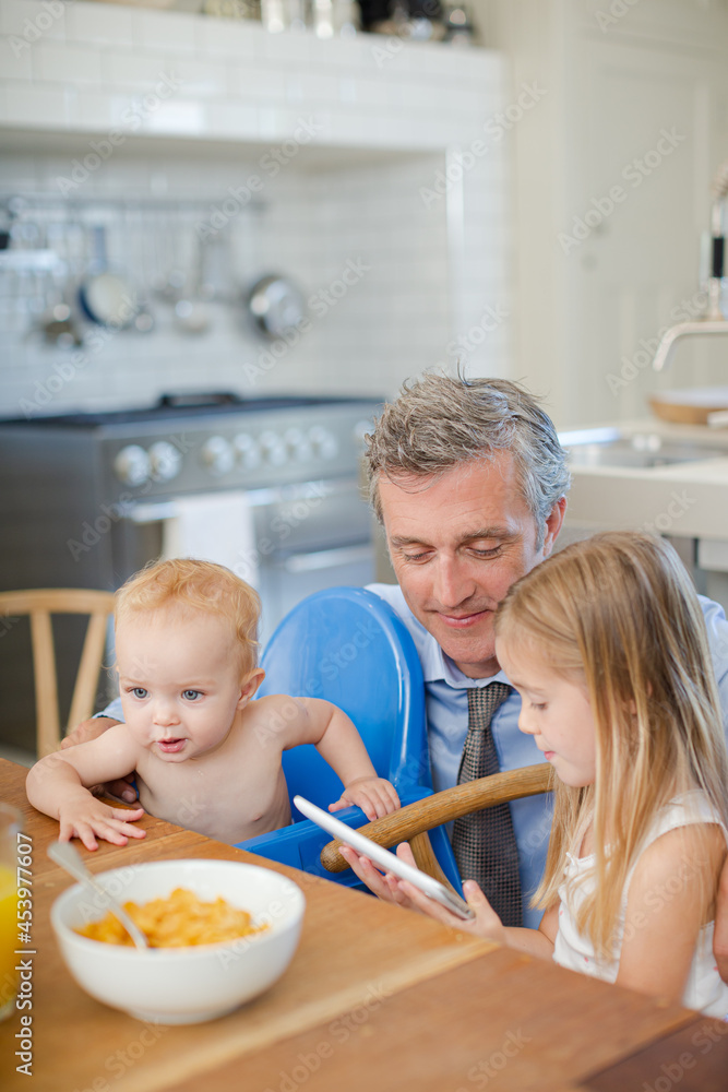 Father and children using digital tablet at table Father and children using digital tablet at table