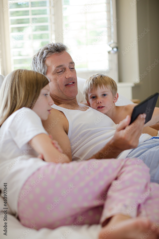 Father and children using digital tablet on bed