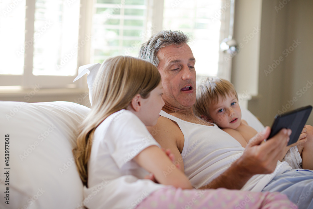 Father and children using digital tablet on bed Father and children using digital tablet on bed