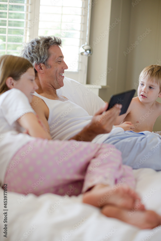 Father and children using digital tablet on bed Father and children using digital tablet on bed