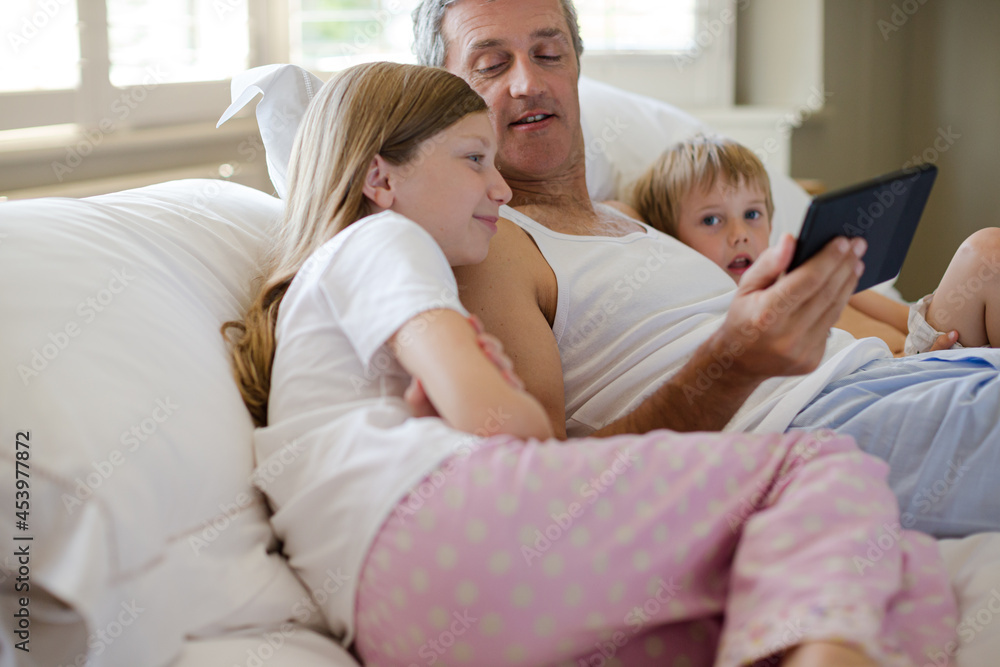 Father and children using digital tablet on bed Father and children using digital tablet on bed