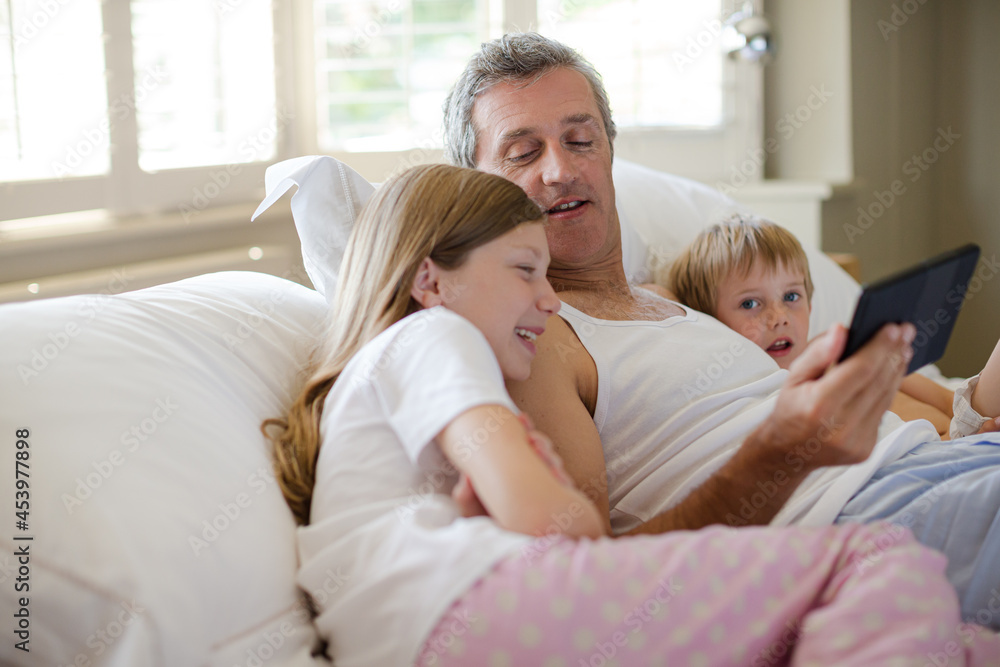 Father and children using digital tablet on bed