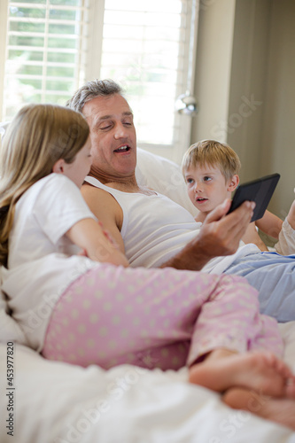 Father and children using digital tablet on bed