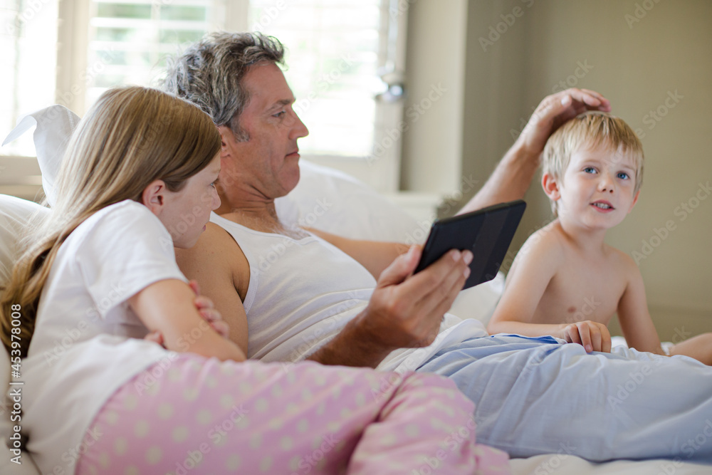 Father and children using digital tablet on bed Father and children using digital tablet on bed