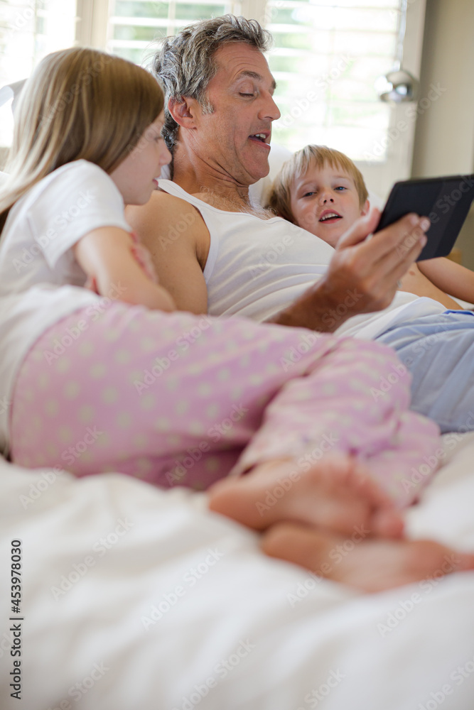 Father and children using digital tablet on bed Father and children using digital tablet on bed