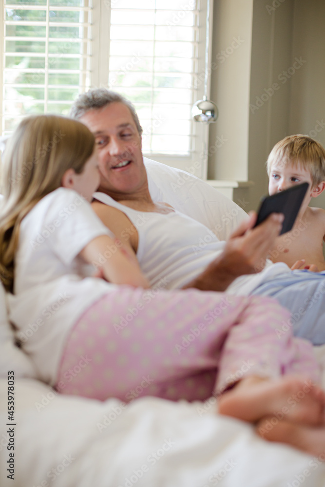 Father and children using digital tablet on bed Father and children using digital tablet on bed