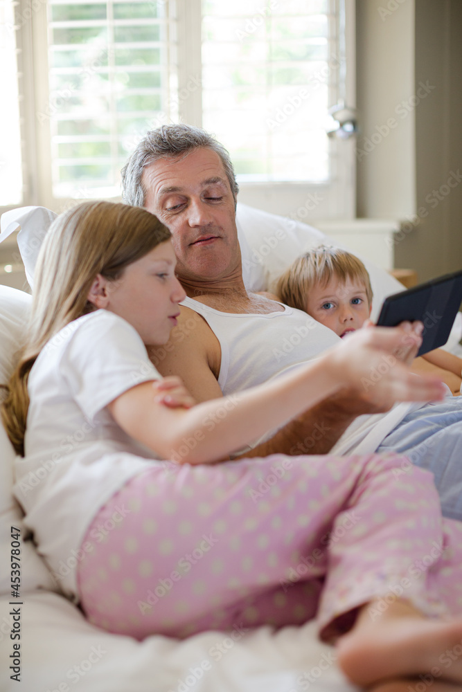 Father and children using digital tablet on bed