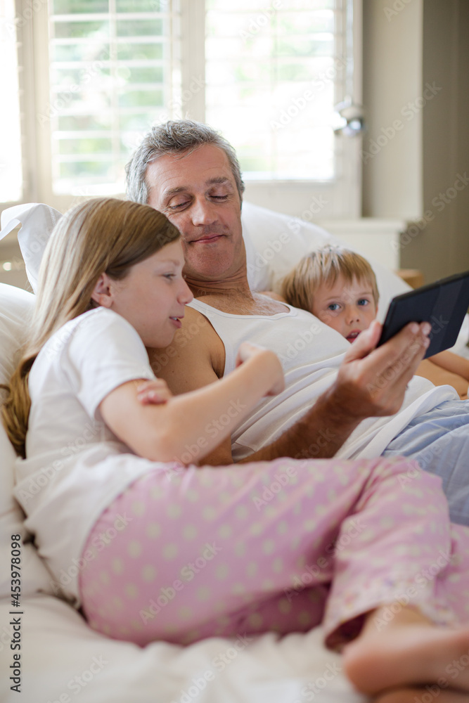 Father and children using digital tablet on bed