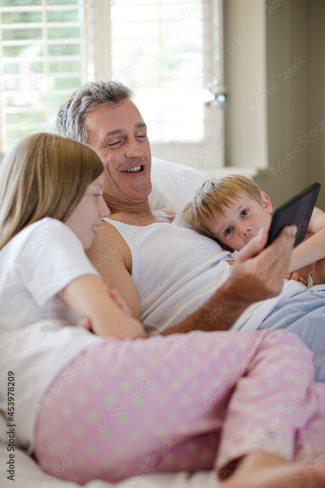 Father and children using digital tablet on bed Father and children using digital tablet on bed