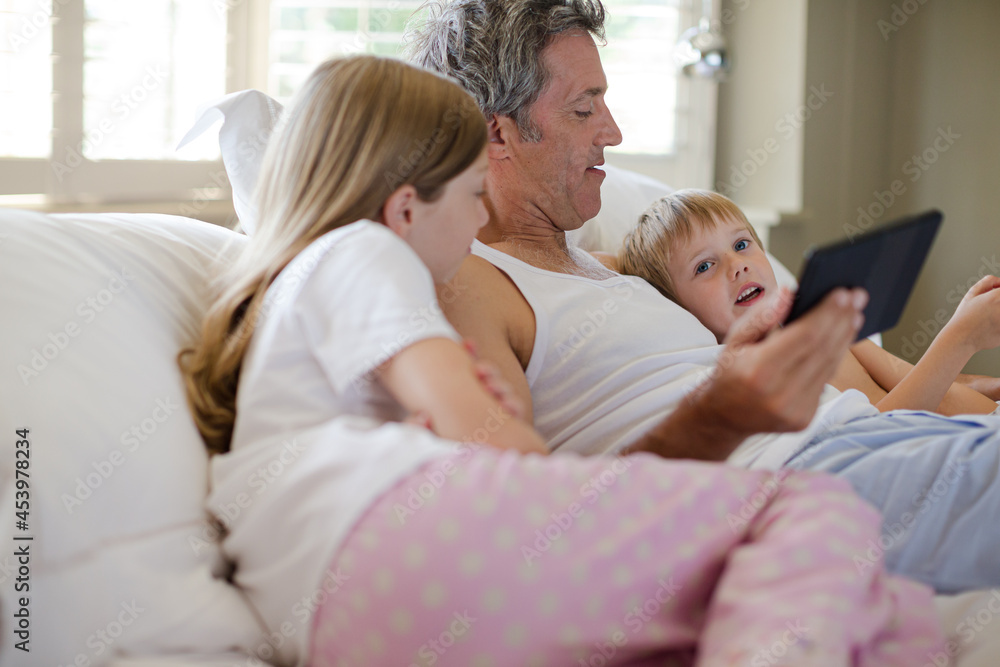 Father and children using digital tablet on bed Father and children using digital tablet on bed