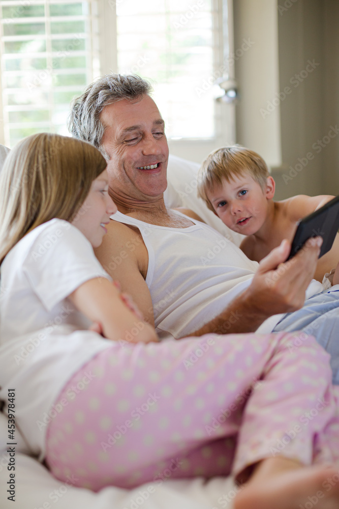 Father and children using digital tablet on bed Father and children using digital tablet on bed