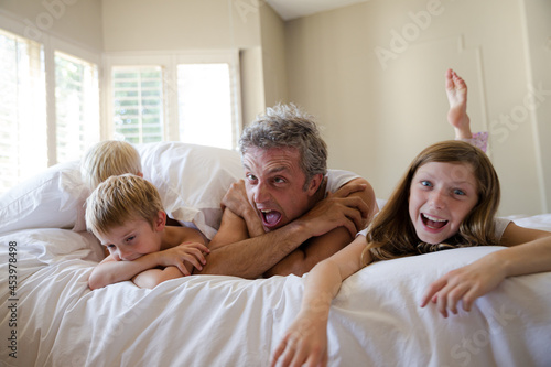 Father and children relaxing on bed © KOTO