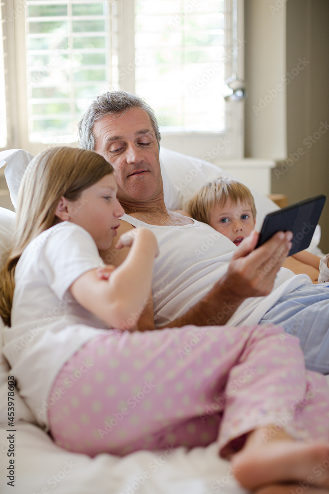 Father and children using digital tablet on bed Father and children using digital tablet on bed