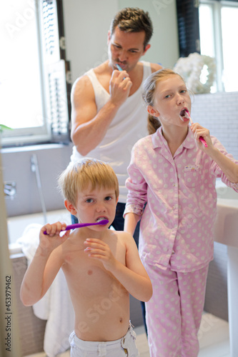 Father and children brushing teeth in bathroom