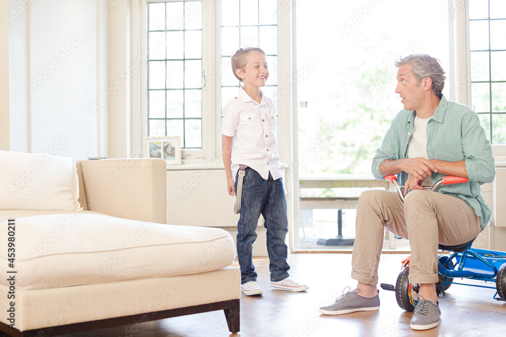 Boy standing with father on tricycle indoors Boy standing with father on tricycle indoors