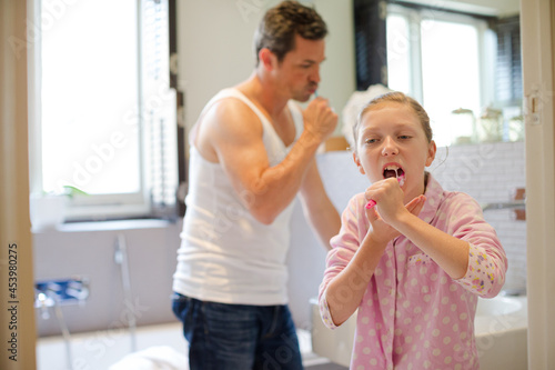 Father and daughter brushing teeth in bathroom