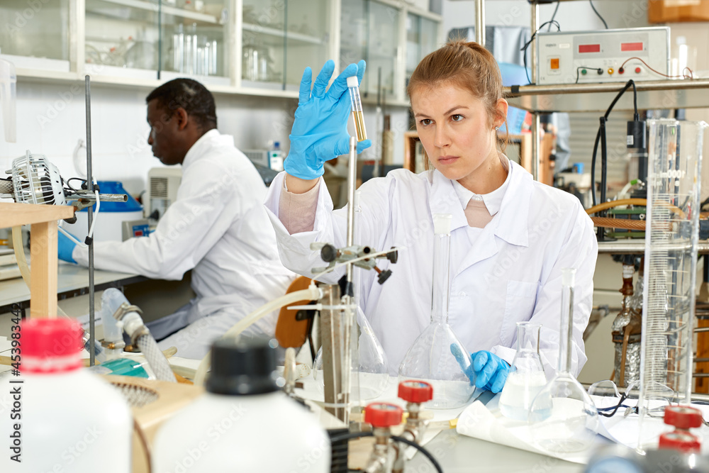 Obraz premium Young female lab technicians working with reagents and test tubes, collegues on background