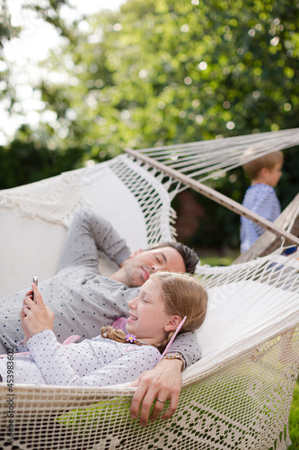 Father and daughter using cell phone in hammock photo