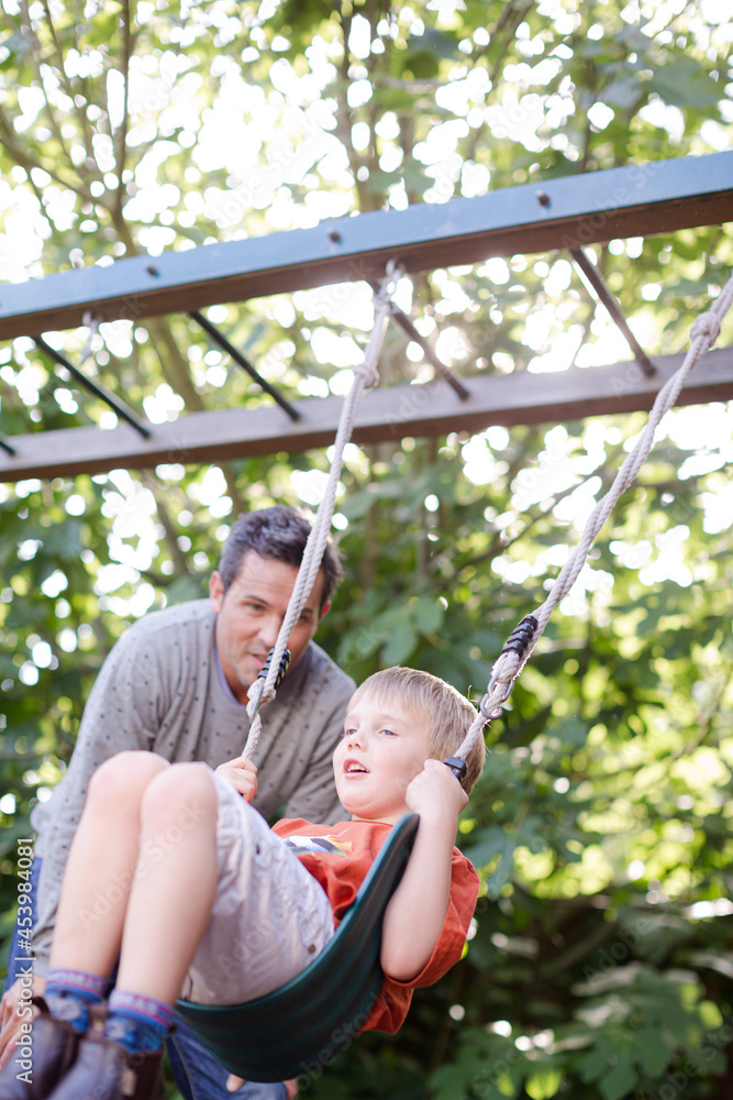 Obraz premium Father pushing son on swing outdoors
