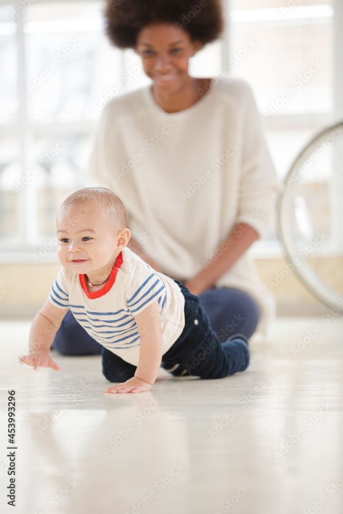 Mother watching baby boy crawl in living room Mother watching baby boy crawl in living room