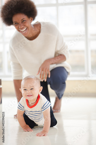 Mother watching baby boy crawl in living room