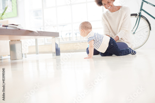 Mother watching baby boy crawl on floor