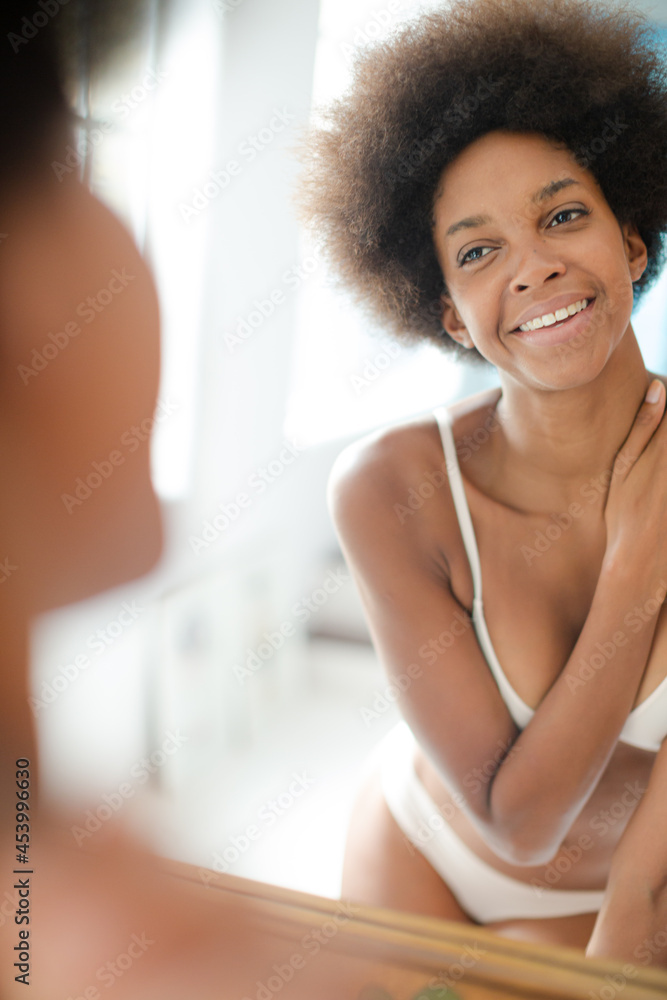 Woman in bra standing at bathroom mirror
