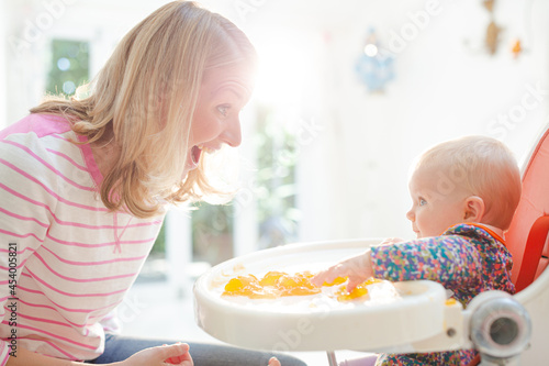 Mother feeding baby girl in high chair