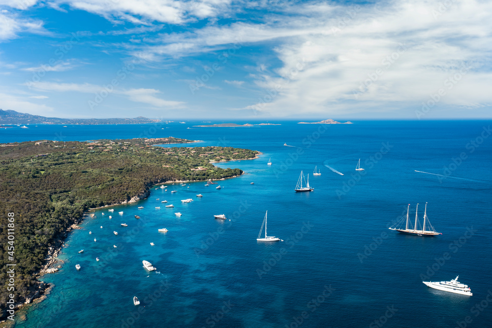 View from above, stunning aerial view of a green coastline with boats and luxury yachts sailing on a turquoise water. Porto Rotondo, Sardinia, Italy.