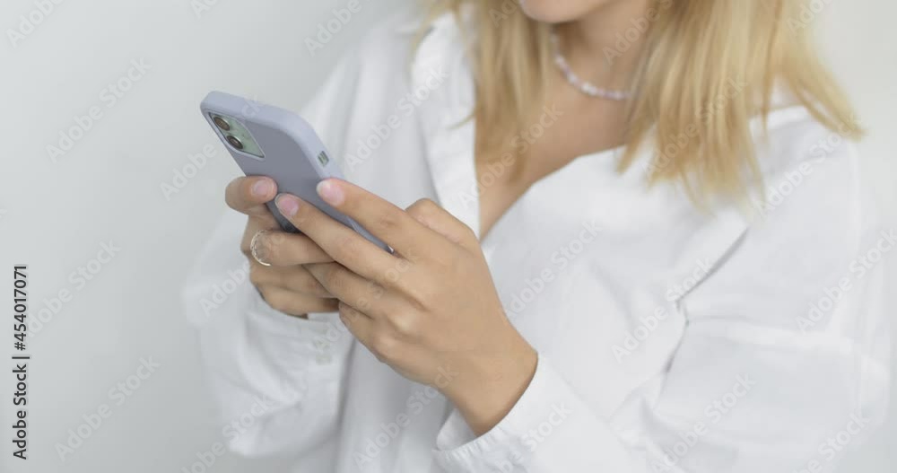 Close-up of a young woman's hands in white shirt with blond hair, on a white background in studio. Using a mobile phone, typing, browsing the pages, chatting. People lifestyle concept. Close-up of a young woman's hands in white shirt with blond hair, on a white background in studio. Using a mobile phone, typing, browsing the pages, chatting. People lifestyle concept.