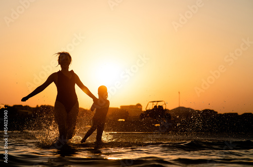 Joyful young mother and her little daughter running and splashing in the sea. Summer vacation and healthy lifestyle concept. Empty space for text
