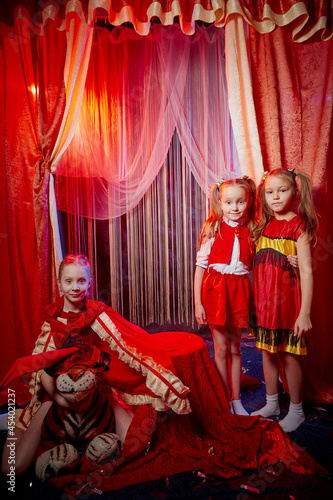 Small girls during a stylized theatrical circus photo shoot in a beautiful red location. Young models posing on stage with curtain. Sisters or female friends together. Twin sisters and a teenager