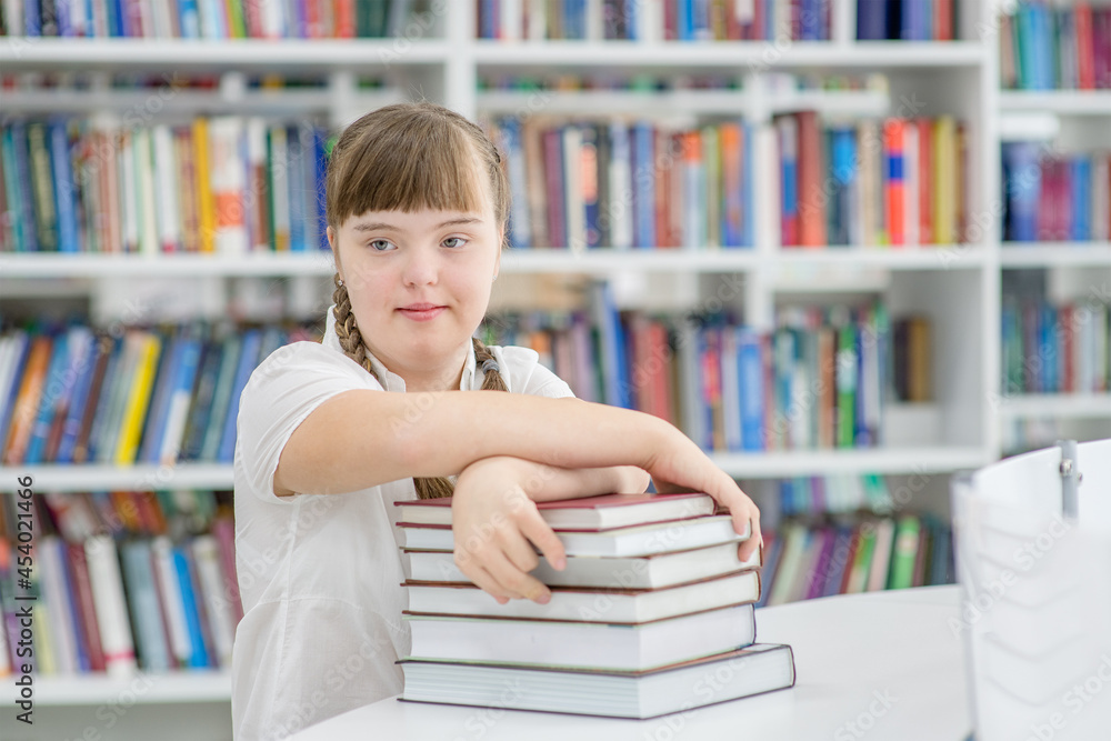 Smart young girl with syndrome down reads a book at library. Education for disabled children concept Smart young girl with syndrome down reads a book at library. Education for disabled children concept