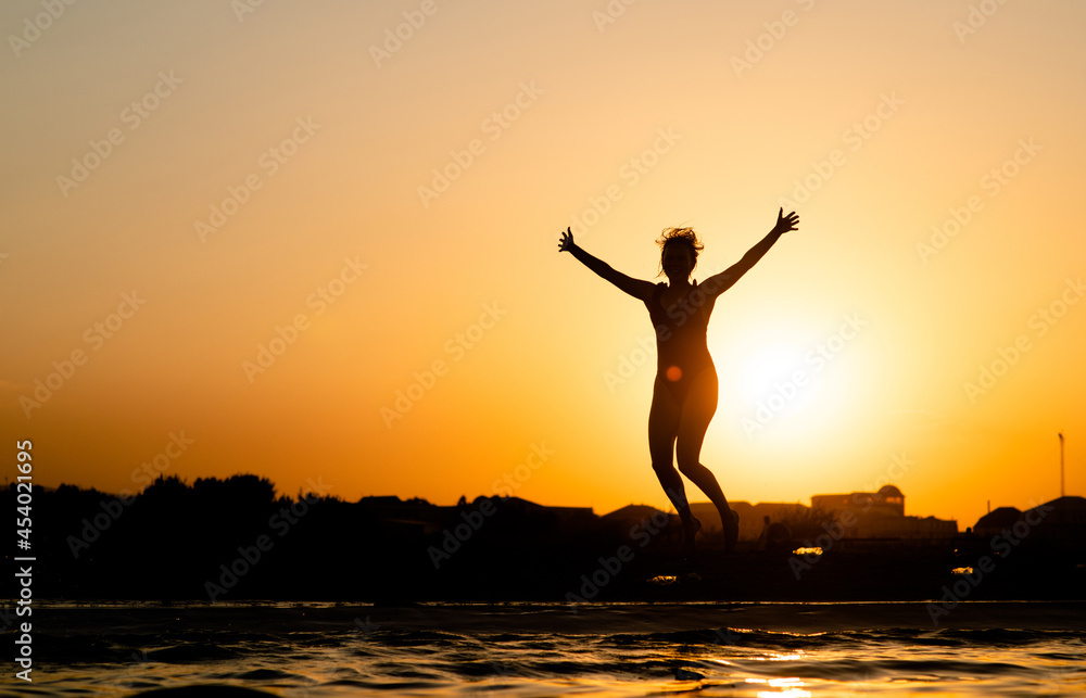 Happy girl having fun and jumps at sunset beach in sunlight. Summer vacation and healthy lifestyle concept. Empty space for text